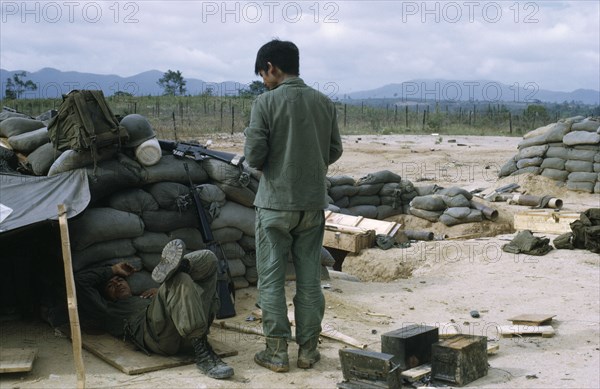 VIETNAM, Central Highlands, Kontum, "Vietnam War. Siege of Kontum. Montagnard soldiers in camp within defensive perimeter, with sand bags and makeshift shelters "