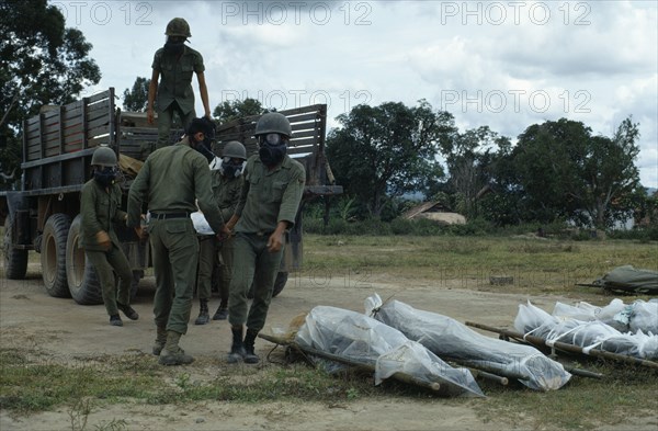 VIETNAM, Central Highlands, Kontum, Vietnam War. Siege of Kontum. Montagnard soldiers wearing gas masks unloading bodies of dead in plastic body bags from truck to be shipped back to their village homes.  Montagnards20092432