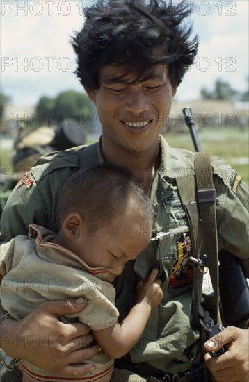 VIETNAM, Central Highlands, Kontum, Vietnam War. Siege of Kontum. Montagnard soldier carrying his baby son