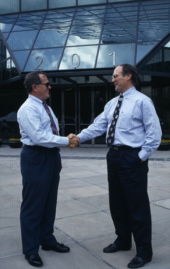 USA, Florida, Orlando, Two businessmen in conversation shaking hands outside modern glass fronted building in downtown business area.