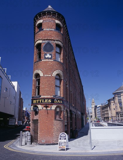 IRELAND, North, Belfast, "Bittles Bar, brick exterior facade, A-board advertising menu and beer barrels at side with the Albert Memorial Clock Tower seen beyond."