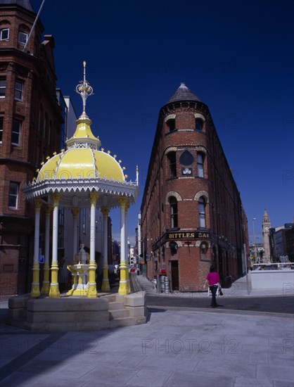 IRELAND, North, Belfast, Victoria Square.  Jaffe Fountain and brick exterior facade of Bittles Bar with the Albert Memorial Clock Tower in the background.