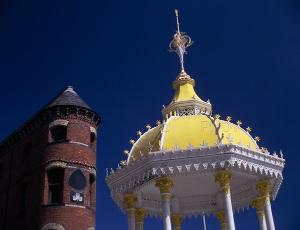 IRELAND, North, Belfast, "Victoria Square.  Detail of yellow and white canopy of the Jaffe Memorial Fountain, constructed in 1874 with top of the brick exterior facade of Bittles Bar behind."