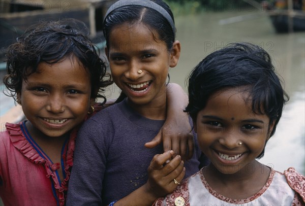 BANGLADESH, Khulna, Char Kukuri Mukuri, Head and shoulders group portrait of three smiling young girls.