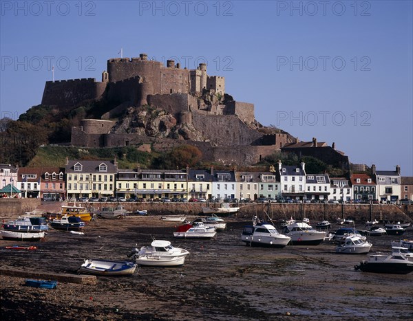 UNITED KINGDOM, Channel Islands, Jersey, Grouville. Gorey Castle or Mont Orgueil set on hill overlooking village buildings and boats in harbour with the tide out. On the east coast.