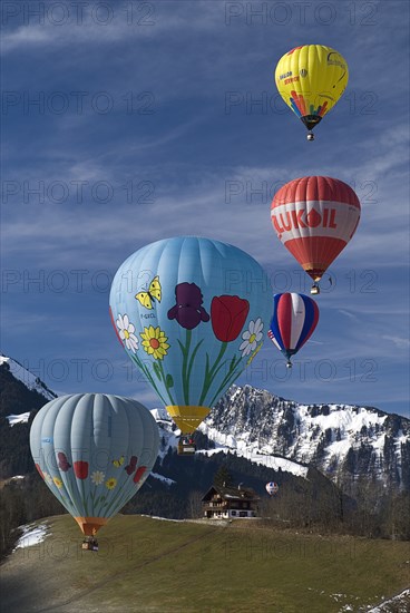 SWITZERLAND, Canton de Vaud, Chateau d'Oex, Hot Air Balloons in flight with mountain backdrop and typical house.