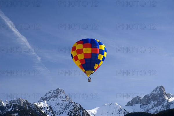 SWITZERLAND, Canton de Vaud, Chateau d'Oex, One Hot Air Balloon in flight above jagged snow covered peaks.