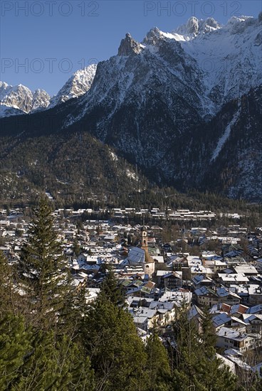 GERMANY, Bavaria, Mittenwald, View over Mittenwald town rooftops from surrounding hillside with snow covered mountains behind