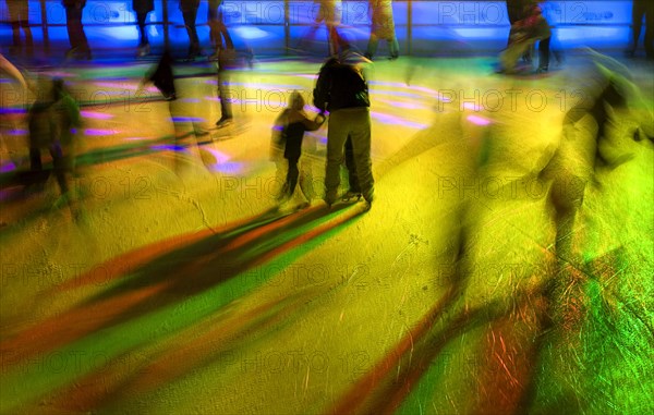 GERMANY, Bavaria, Munich, Ice Skaters in motion blur with multi coloured light on a winter ice rink in the city centre