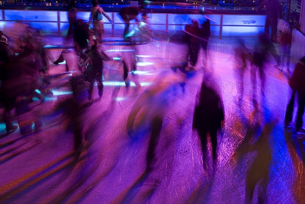 GERMANY, Bavaria, Munich, Ice Skaters in motion blur with multi coloured light on a winter ice rink in the city centre