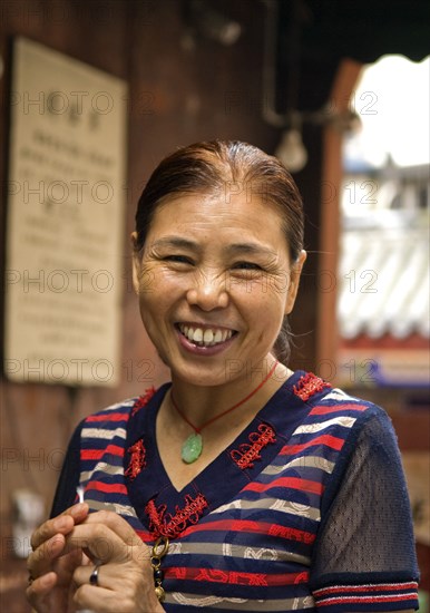 CHINA, Sichuan Province, Chongqing, "Portrait of a smiling woman, an Arhat Temple incense stick maker in outer courtyard of this 1000 year old temple much of which survived the Cultural Revolution"