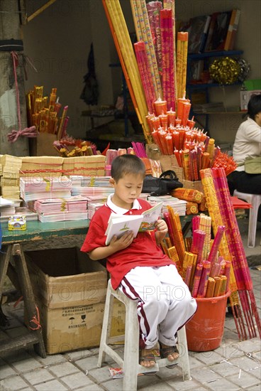CHINA, Sichuan Province, Chongqing, Boy incense seller reading book outside the Arhat Temple in downtown Chongqing