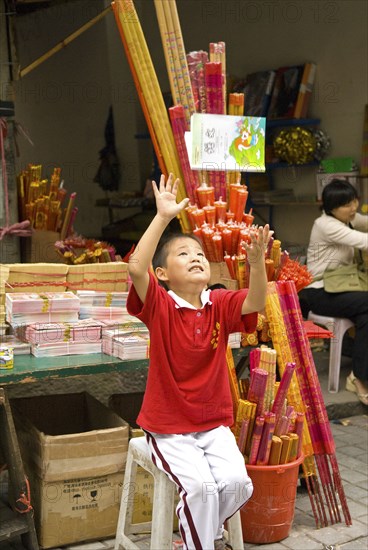 CHINA, Sichuan Province, Chongqing, Boy incense seller throws his book up in glee outside the Arhat Temple in downtown Chongqin
