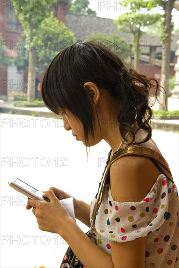 CHINA, Sichuan Province, Chongqing, "Girl using a mobile phone, a local tour guide at the 1500 year old Baolun Si Temple which dates back to the Western Wei dynasty"