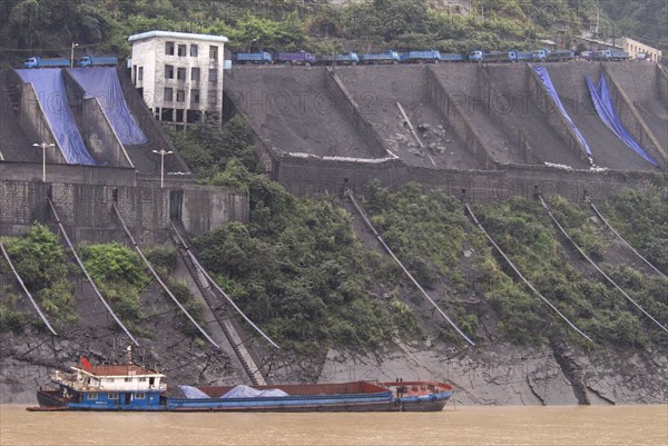 CHINA, Hubei , Sandouping, Industrial complex in the Wu Gorge. Line of trucks bring coal from the mines and dump into bunkers from where it flows through pipes to coal barges waiting below on the Yangtze River