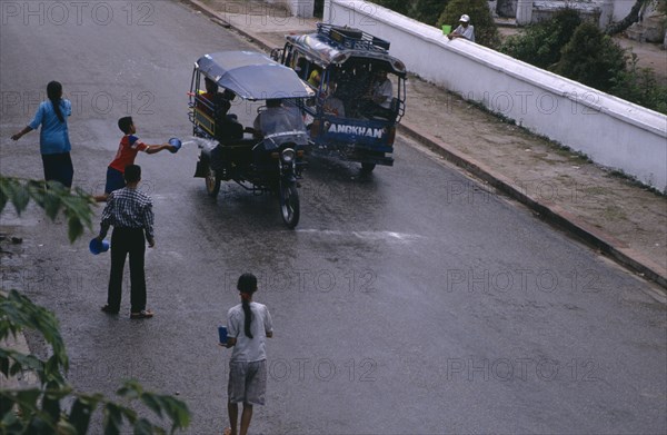 LAOS, Luang Phrabang, Children celebrating the lunar New Year throwing water at passing tuk tuks.