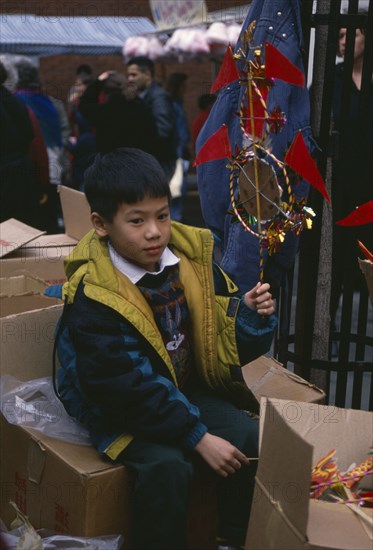 ENGLAND, London, Chinese New Year, Young boy sitting on boxes holding up decoration for New Year celebrations.