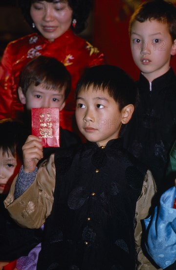ENGLAND, London, Chinese New Year, "Children celebrating the Year of the Tiger in Chinatown, Soho.  Small boy holding up laisee or lucky packet containing money and decorated with lucky symbols."