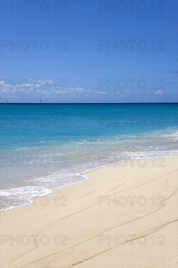 WEST INDIES, St Vincent And The Grenadines, Canouan, South Glossy Beach in Glossy Bay with waves breaking on the shoreline of the turqoise sea and yachts on the horizon