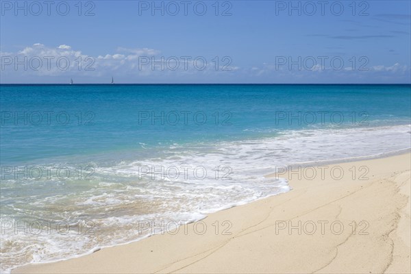 WEST INDIES, St Vincent And The Grenadines, Canouan, South Glossy Beach in Glossy Bay with waves breaking on the shoreline of the turqoise sea and yachts on the horizon