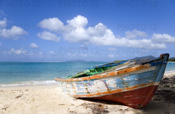 WEST INDIES, Grenada, Carriacou, Waves breaking on Paradise Beach at L'Esterre Bay with an old fishing boat on the shore and the turqoise sea and Sandy Island sand bar beyond.
