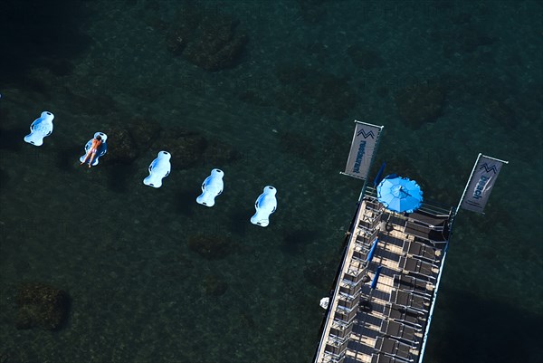 20093624 ITALY Campania Sorrento Solitary figure lounging on beach tub in Sorrento Harbour with deck on left