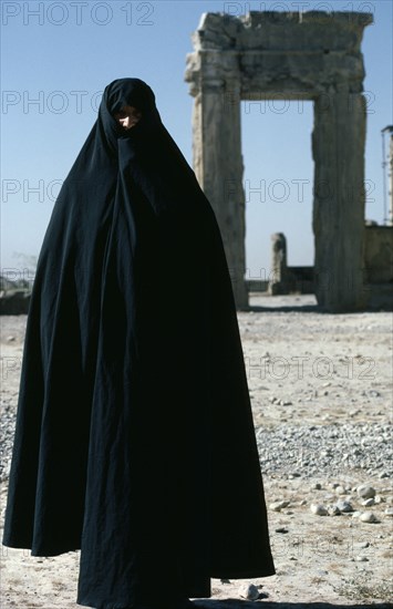 IRAN, Fars Province , Persepolis, Full length standing portrait of a woman wearing a black Chador at Persepolis
