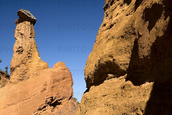 FRANCE, Provence Cote d’Azur, Vaucluse, "Colorado Provencal.  Cheminee de Fee or Fairy Chimneys.  Capped, eroded ochre rock pinnacle seen from park trail against cloudless blue sky."