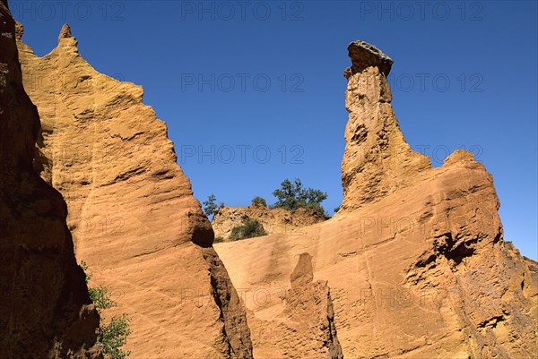 FRANCE, Provence Cote d’Azur, Vaucluse, "Colorado Provencal.  Cheminee de Fee or Fairy Chimneys.  Capped, eroded, ochre rock pinnacle, angled view against blue sky from park trail "