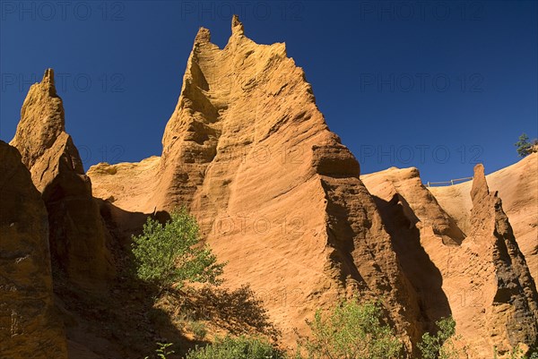 FRANCE, Provence Cote d’Azur, Vaucluse, Colorado Provencal.  Cheminee de Fee or Fairy Chimneys.  Looking up eroded ochre cliff face topped with jagged peaks from park trail below.