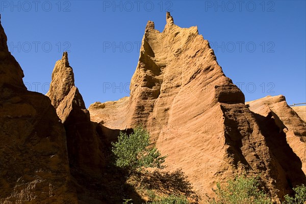 FRANCE, Provence Cote d’Azur, Vaucluse, Colorado Provencal.  Cheminee de Fee or Fairy Chimneys.  Looking up eroded ochre cliff face topped by jagged peaks from park trail below.