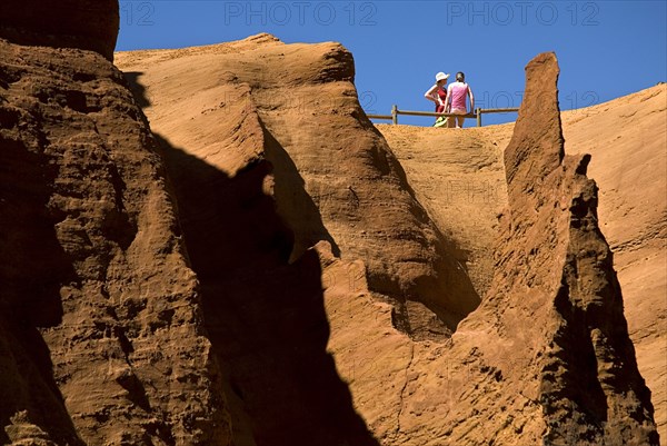 FRANCE, Provence Cote d’Azur, Vaucluse, Colorado Provencal.  Cheminee de Fee or Fairy Chimneys.  Two tourists admire the view from top of eroded ochre rock.