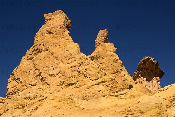 FRANCE, Provence Cote d’Azur, Vaucluse, "Colorado Provencal.  Cheminee de Fee or Fairy Chimneys.  Looking up at eroded, capped rock pinnacles on summit of ochre cliff from below."