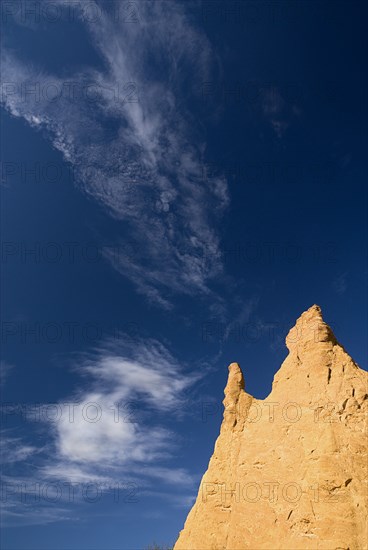 FRANCE, Provence Cote d’Azur, "Colorado Provencal.  Cheminee de Fee or Fairy Chimneys.  Dramatic sky with high, windswept clouds over jagged peak of ochre rock."