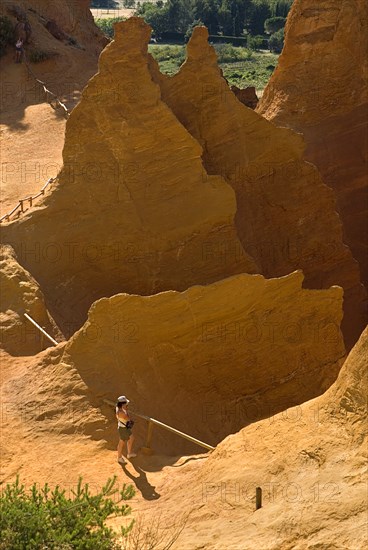 FRANCE, Provence Cote d’Azur, Vaucluse, Colorado Provencal.  Cheminee de Fee or Fairy Chimneys.   A tourist standing at park viewpoint surrounded by peaks and gullys of eroded ochre rock.