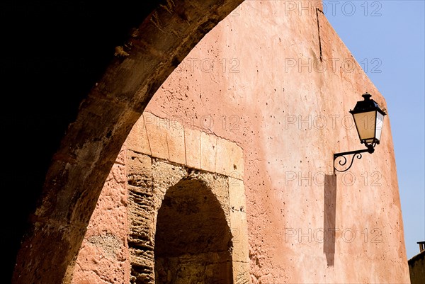 FRANCE, Provence Cote d’Azur, Vaucluse, Roussillon.  Architectural detail of archway framing street light on red exterior wall of town building.