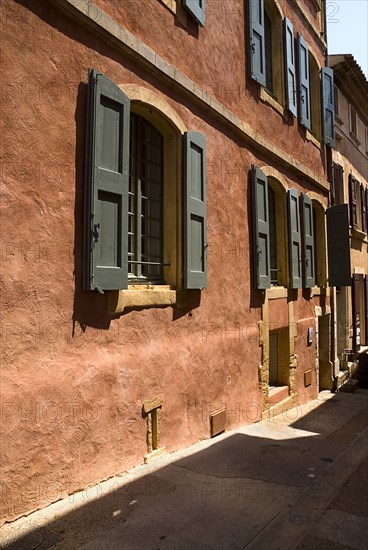 FRANCE, Provence Cote d’Azur, Vaucluse, Roussillon.  Typical red exterior wall of building with painted window shutters and step down to street.