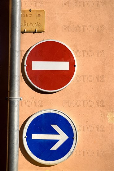 FRANCE, Provence Cote d’Azur, Vaucluse, Roussillon.  Prohibitive and directional road signs on ochre coloured wall in the town square.