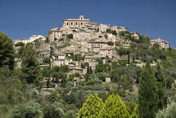 FRANCE, Provence Cote d’Azur, Vaucluse, Gordes.  View of hilltop village from the road below with church at summit.
