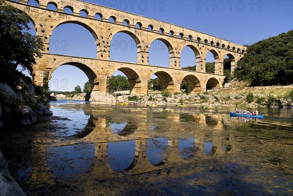 FRANCE, Provence Cote d’Azur, Gard, Pont du Gard.  View from west side of the Roman aqueduct in glowing evening light with passing canoes and reflection in water below.