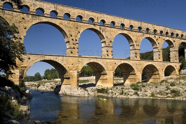 FRANCE, Provence Cote d’Azur, Gard, Pont du Gard.  View from west side of the Roman aqueduct in glowing evening light with passing canoe and reflection in the water below.
