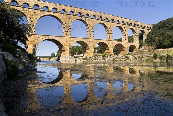 FRANCE, Provence Cote d’Azur, Gard, Pont du Gard.  View from west side of the Roman aqueduct in glowing evening light with reflection in the water below.