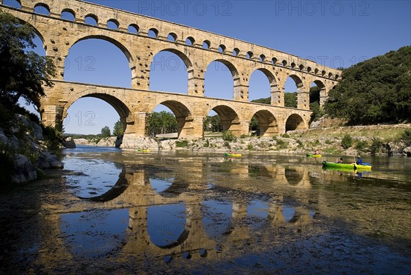 FRANCE, Provence Cote d’Azur, Gard, Pont du Gard.  View from west side of the Roman aqueduct in glowing evening light with passing canoes and reflection in the water below.