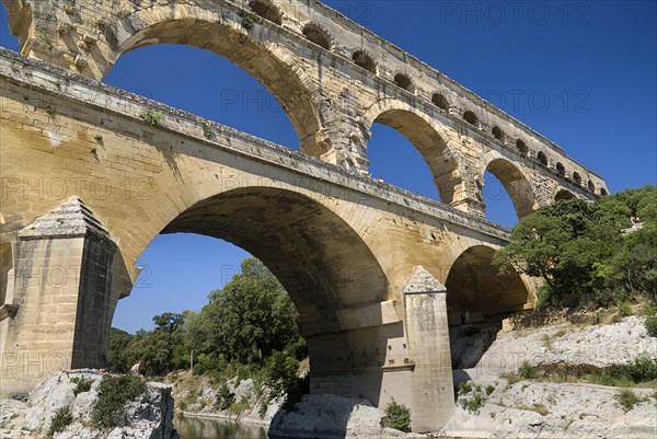 FRANCE, Provence Cote d’Azur, Gard, Pont du Gard Roman aqueduct.  Angled view of the east side in the morning showing section of three tiers of arches and rocky bank.