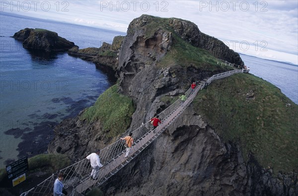 NORTHERN IRELAND, County Antrim, Ballintoy, Carrick-a-Rede Rope Bridge. Vistors walking over rope bridge linking a rocky island to cliffs.