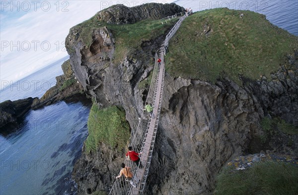 NORTHERN IRELAND, County Antrim, Ballintoy, Carrick-a-Rede Rope Bridge. Vistors walking over rope bridge linking a rocky island to cliffs.