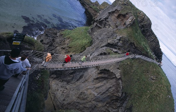 NORTHERN IRELAND, County Antrim, Ballintoy, Carrick-a-Rede Rope Bridge. Vistors walking over rope bridge linking a rocky island to cliffs.