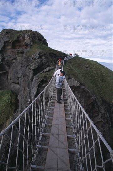 NORTHERN IRELAND, County Antrim, Ballintoy, Carrick-a-Rede Rope Bridge. Vistors walking over rope bridge linking a rocky island to cliffs.