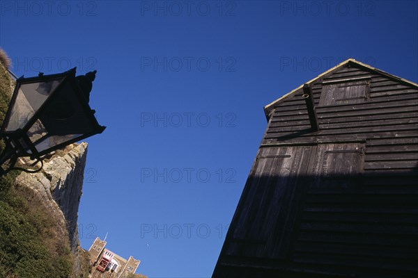 ENGLAND, East Sussex, Hastings, The Net Shops. Tall black wooden huts used for storing fishing nets. Funicular railway behind.