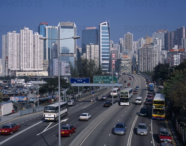 CHINA, Hong Kong, Causeway Bay, Multi-lane city road busy with traffic beside Causeway Bay boats and typhoon shelter with high rise city buildings beyond.